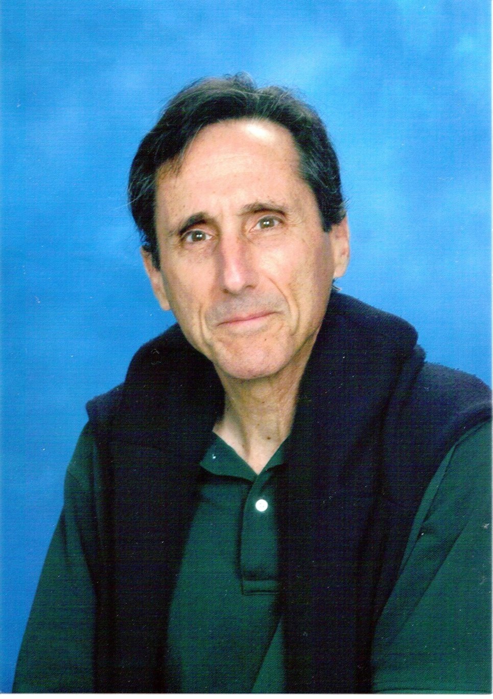 Portrait of author Bruce Silton in a green polo shirt with a navy sweater over his shoulders, against a blue background